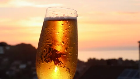 Beer glass being held in front of Sunset in Devon, UK Stock Footage 242072897