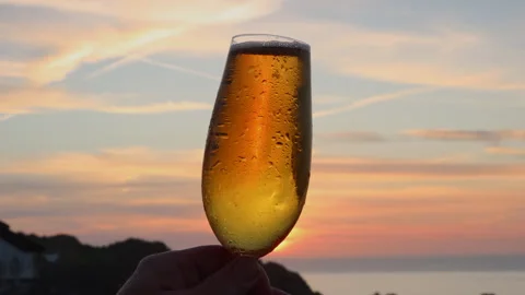 Beer glass being held in front of Sunset in Devon, UK Stock Footage 242074722