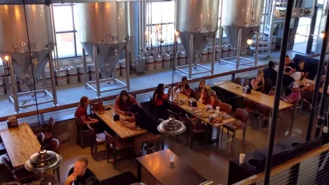 Beer kegs line the wall in front of huge fermentation tanks in a brewery-eatery Vídeo Stock 226434793