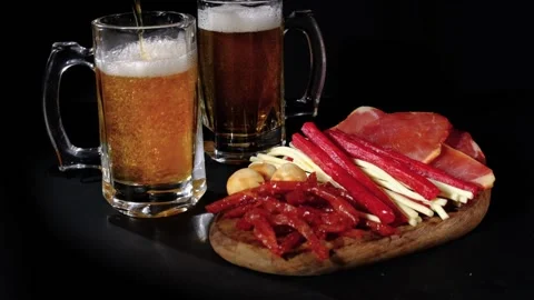 Beer pours into a mug behind snacks. 120 fps Stock Footage 214758019