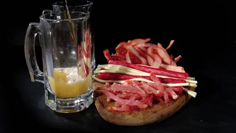 Beer pours into a two mugs behind snacks. 120 fps Stock Footage 214757714