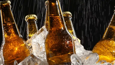 Beer stands in the ice, water flows from above, splashes fall on the glass Stock Footage