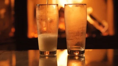 Beer in two glasses on table in front of burning fireplace. Stock Footage 82542198