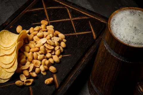 Beer in a wooden mug with peanuts and chips on a board Stock Photos