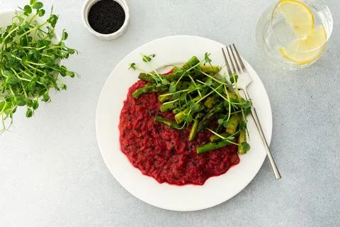 Beetroot risotto with rice and sesame seeds, baked asparagus with microgreens Stock Photos
