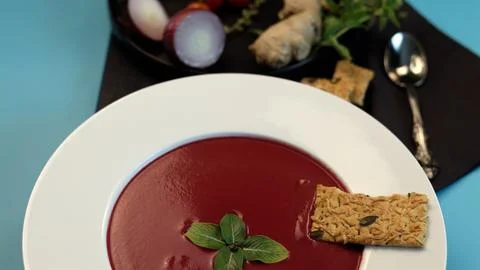 Beetroot soup served in pristine white plate contrasts strikingly with blue Stock Photos