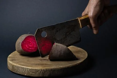 Beets, cut in half. A hand cuts beets with a rusty kitchen hatchet. Stock Photos