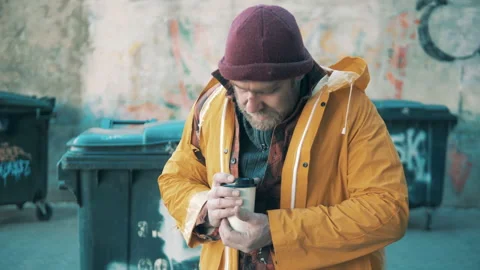 A beggar is drinking coffee next to the waste bins Vidéo 168128794