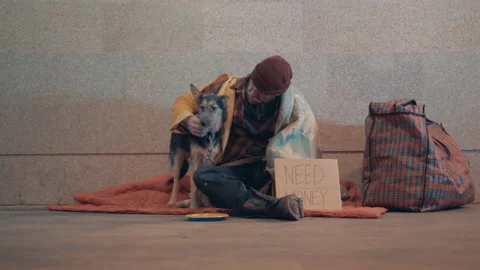 A beggar is stroking his dog while sitting on the ground Vidéo 168129037