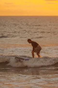 Beginner surfer learns to row and ride on a training board in small waves in the Stock Photos