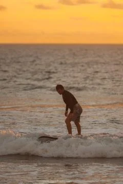 Beginner surfer learns to row and ride on a training board in small waves in the Stock Photos