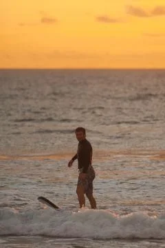 Beginner surfer learns to row and ride on a training board in small waves in the Stock Photos