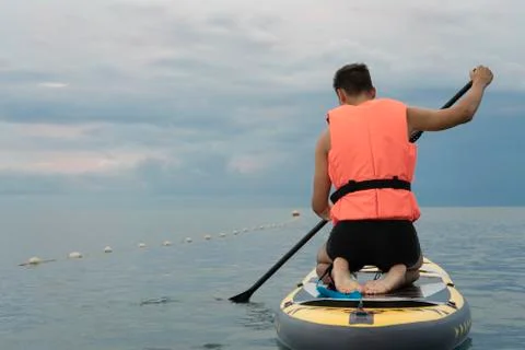 Beginner surfer in the life jacket is preparing to learn to sup surf on calm  Stock Photos