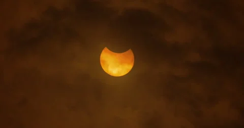 The beginning of a partial solar eclipse behind thick clouds, October Stock Footage 253372799