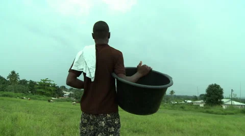 FROM BEHIND: ADEISO MAN CARRIES BUCKET DOWN PATH Stock Footage 58069892