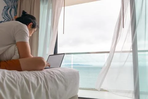 Behind angle of man work on the bed with sea view. Concept of workation. Stock-Fotos