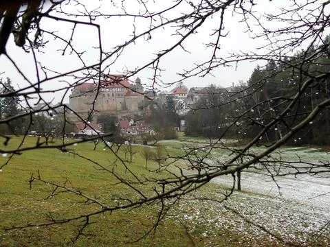 Behind the branches of the tree, you can see a field covered with frost Stock Photos
