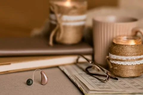 Behind-the-ear hearing aid lying near warm candles, a notebook, and reading g 库存照片