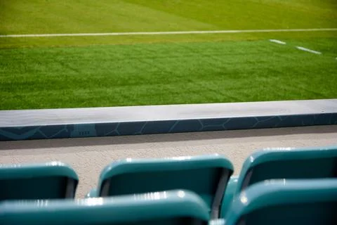 Behind empty back blue plastic seats against backdrop of a green football field Stock Photos