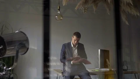Behind the glass a man looks at a folder with documents in the office 스톡 동영상 110945555