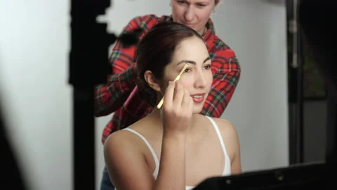 Behind the scenes photo shoot model touches up makeup as hairstylist fixes hair 스톡 동영상 193896437
