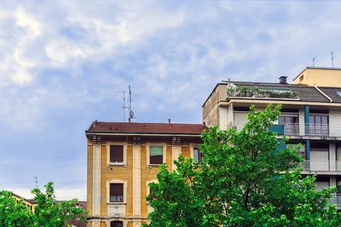 Behind the spring green maple leaves, an old yellow stone residential buildin Stock Photos