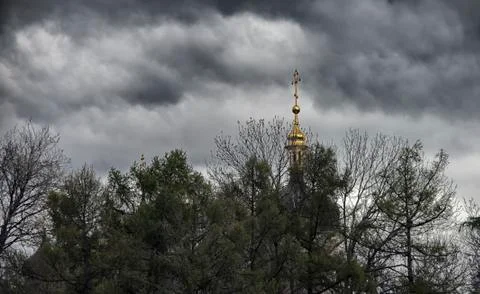Behind the trees, against the background of clouds, is a golden cross. Foto stock