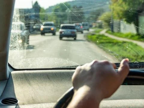 Behind wheel to dirty windshield, hand of woman on steering wheel, heavy traf Stock Photos