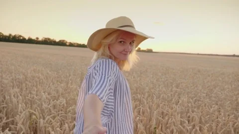 Behind you in the field of wheat, carry away by the hand. A woman leads a Video stock 78534723