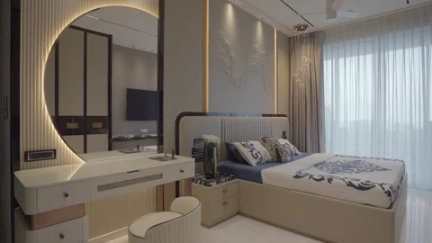 Beige and navy bed beside a white vanity with circular backlit mirror, floral Stock Footage 328486184