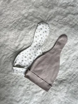 Beige and white caps with stars are lying on a light plaid bed in the room... Stock Photos