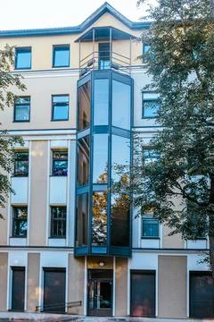 Beige apartment building with external glass elevator shaft and trees Stock Photos
