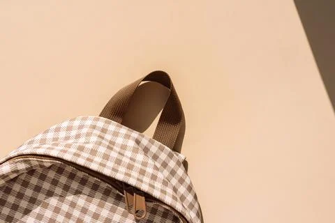 Beige checkered school backpack in warm sunlight with copy space, back to Stock Photos
