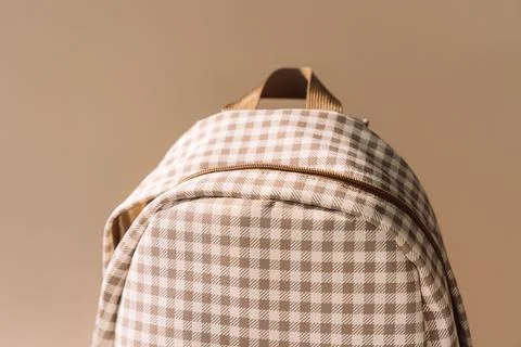 Beige checkered school backpack in warm sunlight, minimal back to school Stock Photos