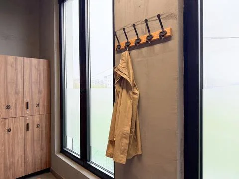 Beige coat hanging on wall hooks near window inside modern locker room interi Stock Photos