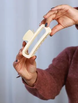 Beige rectangular claw clip held in hand, modern hair accessory Stock Photos