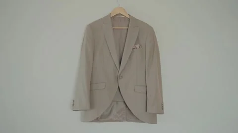 Beige Single Button Groom Suit Jacket on Wooden Hanger Against Gray Wall 库存影片 332920425