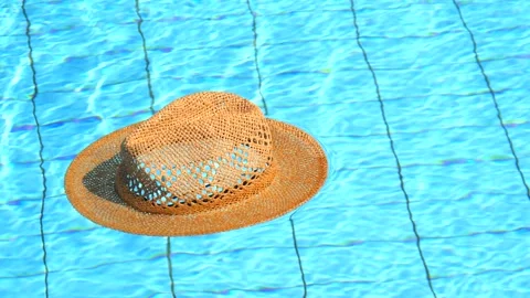 A beige straw summer hat swims in an empty blue water pool. The concept Stock Footage 147948861
