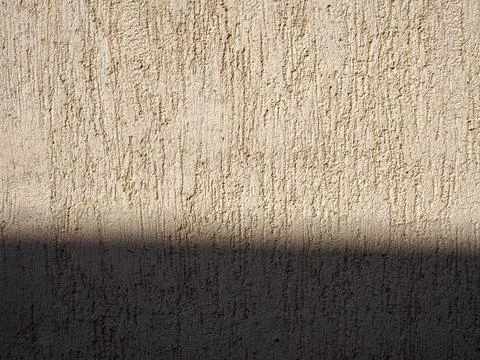 Beige textured wall with shadow and plaster applied with putty knife in irreg Stock Photos