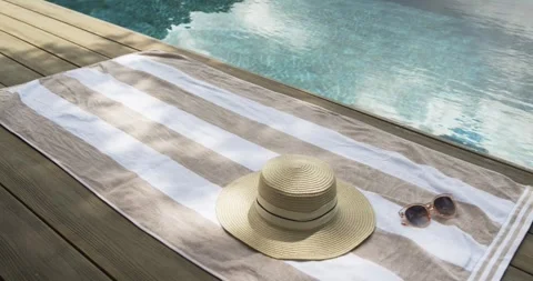 Beige towel with straw hat and sunglasses is resting on deck while breeze is Stock Footage 336609575