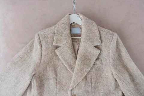 Beige wool polyester blend coat jacket with wide lapel on hanger over soft pink Stock Photos