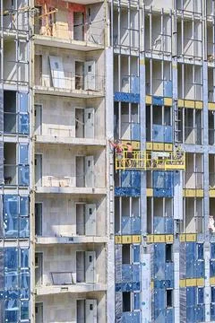 Being on construction cradle, builders insulate walls of facade of multi-stor Stock Photos