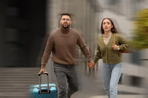 Being late. Young couple with suitcase running on city street. Motion blur .. Stock Photos
