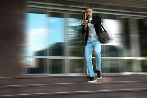 Being late. Young man checking time while running down stairs outdoors. Mot.. Stock Photos