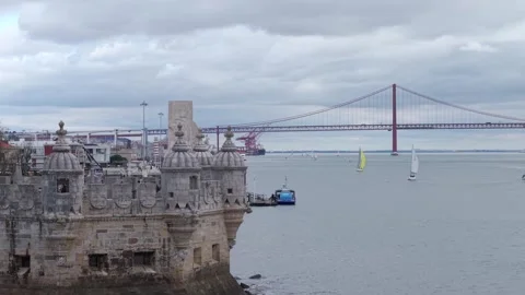 Belem Tower on Tagus river bank, Ponte 25 de Abril suspension bridge in Stock Footage 334636855