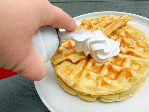 Belgian waffles and a hand squeezing white cream onto them. 写真素材