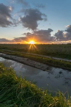 Below a cloud bank the sun sets over the dutch countryside Stock Photos