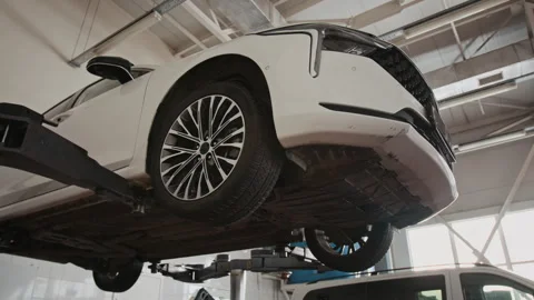 Below View of White Car on Hydraulic Lift during Suspension Diagnostics Stock Footage 329406964