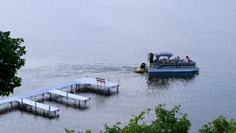 BEMIDJI, MN - 2 JUN 2023: Family in pontoon sail past dock on lake. Stock Footage 251756876