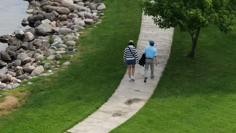 BEMIDJI, MN - 3 JUN 2023: Couple walking on sidewalk past tree. Stock Footage 251756875